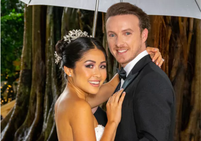 A bride and groom posing for a photo outside in the rain
