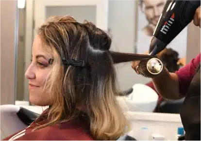 HairClub - EXT Scalp Treatments - a woman sitting in a HairClub salon getting her hair blown dry and styled by a professional HairClub stylist.